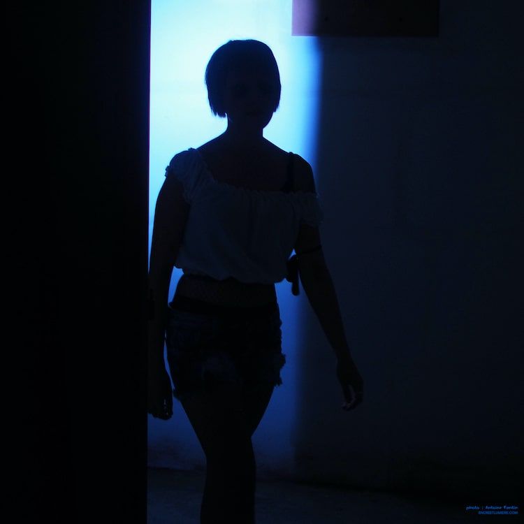 Silhouette de jeune femme aux cheveux courts en contre-jour avec lumière bleue. Photo : Antoine Fantin