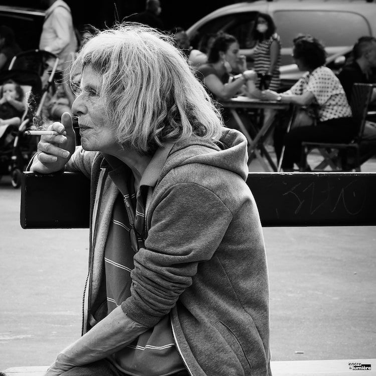 Vieille femme qui fume sur un banc