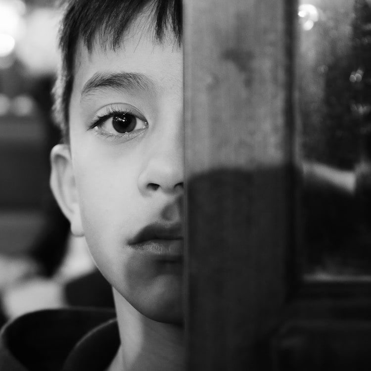 Enfant de 9 ans, visage à moitié caché derrière une poutre