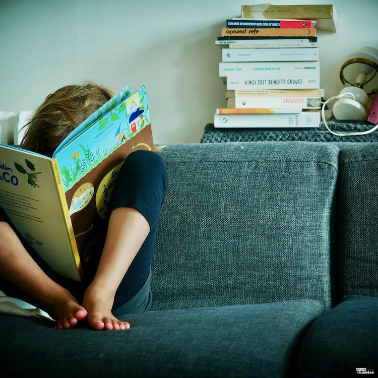 Enfant de 7 ans lisant un livre dans un canapé.