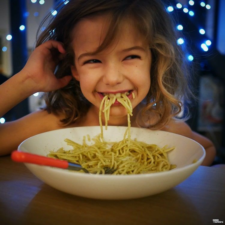 Enfant mangeant un plat de spaghettis en riant.