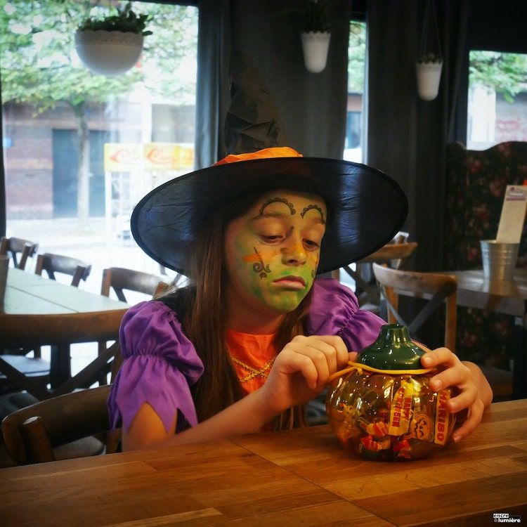 Halloween : Enfant fille qui boude déguisée en sorcière avec sac de bonbons. 