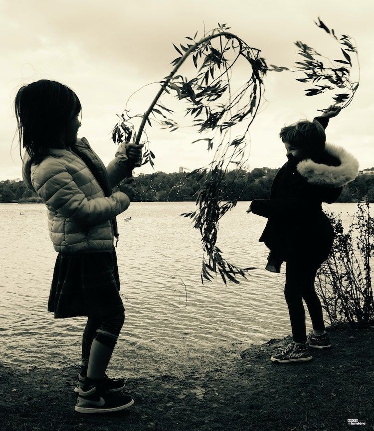 Deux enfants s'amusant avec des branches au bord d'un lac. Photographe enfant Normandie.