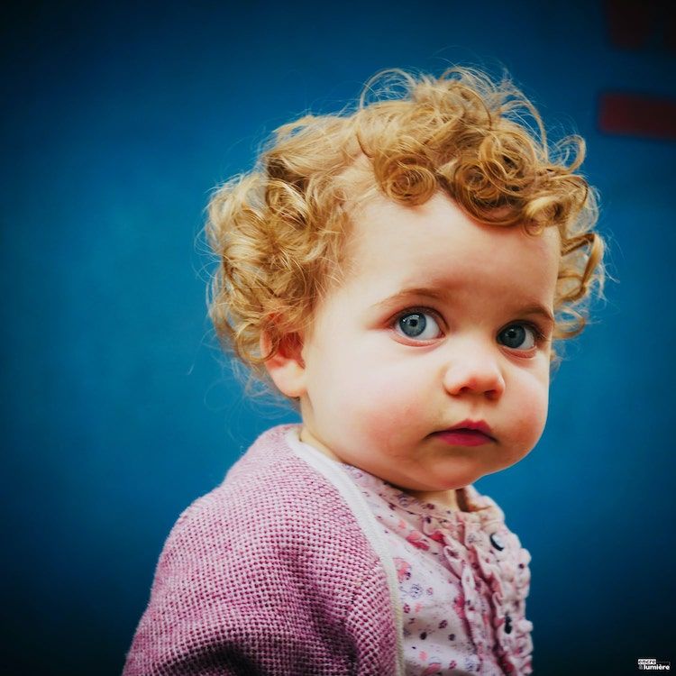 portrait d'un bébé aux yeux bleus, cheveux roux sur fond bleu.