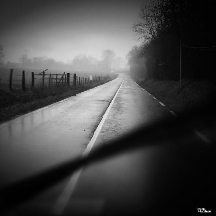 Route sous la pluie, en noir et blanc. photo prise derrière le pare-brise.
