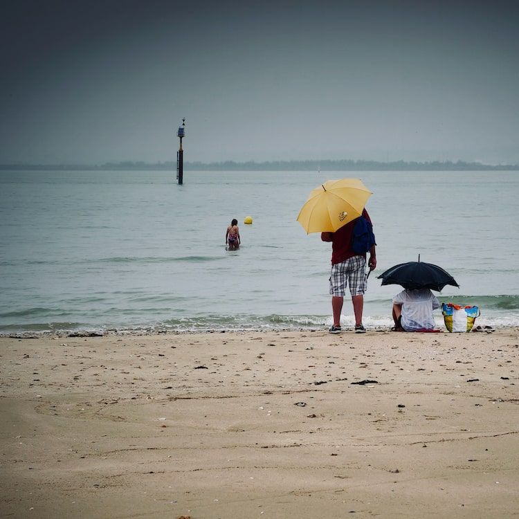 Couple avec parapluies jaune sur une plage sous la pluie. Honfleur. Série "Un temps de chien" de Antoine Fantin.