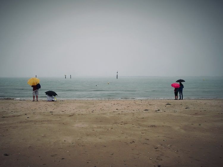 Deux couples avec des parapluies sur une plage sous la pluie. Honfleur. Série "Un temps de chien" de Antoine Fantin.
