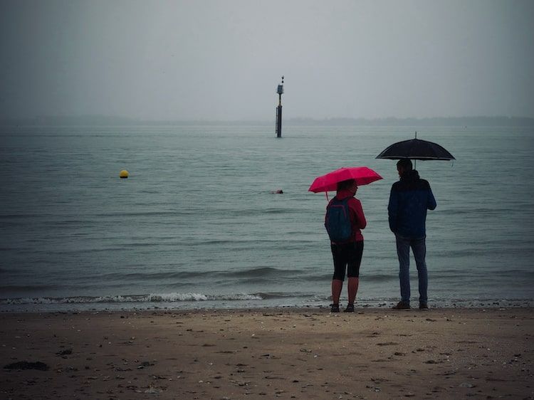 Couples avec parapluie rose sur une plage sous la pluie. Honfleur. Série "Un temps de chien" de Antoine Fantin.