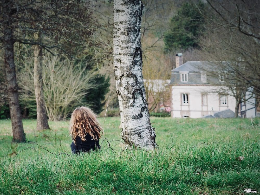 Enfant aux longs cheveux blonds assise de dos dans l'herbe. Photo : Antoine Fantin "Encre & Lumière"